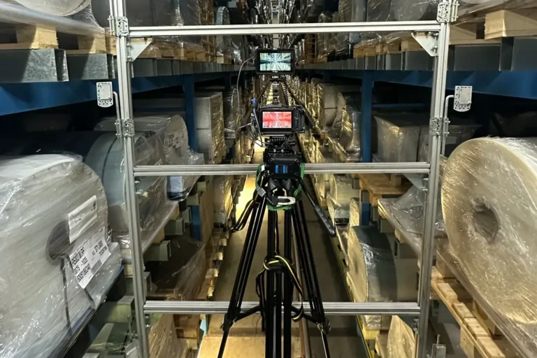 videocamera su treppiede tra le scaffalature di un magazzino automatico, riprese industriali in sicurezza
